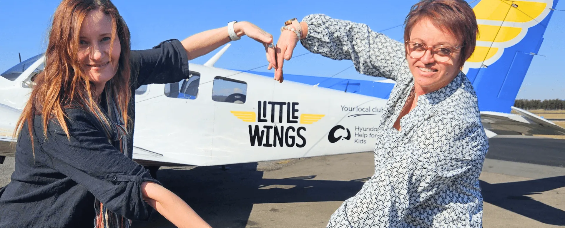 two of the Hunter team making a heart shape with their arms in front of the Little Wings plane