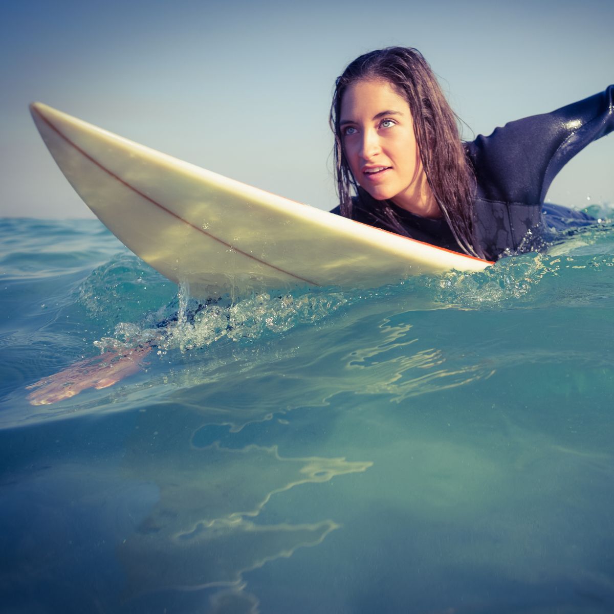 a surfer in a wetsuit paddling in the sea