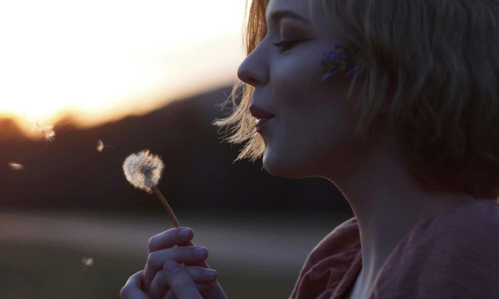 Woman blowing dandelion at dusk