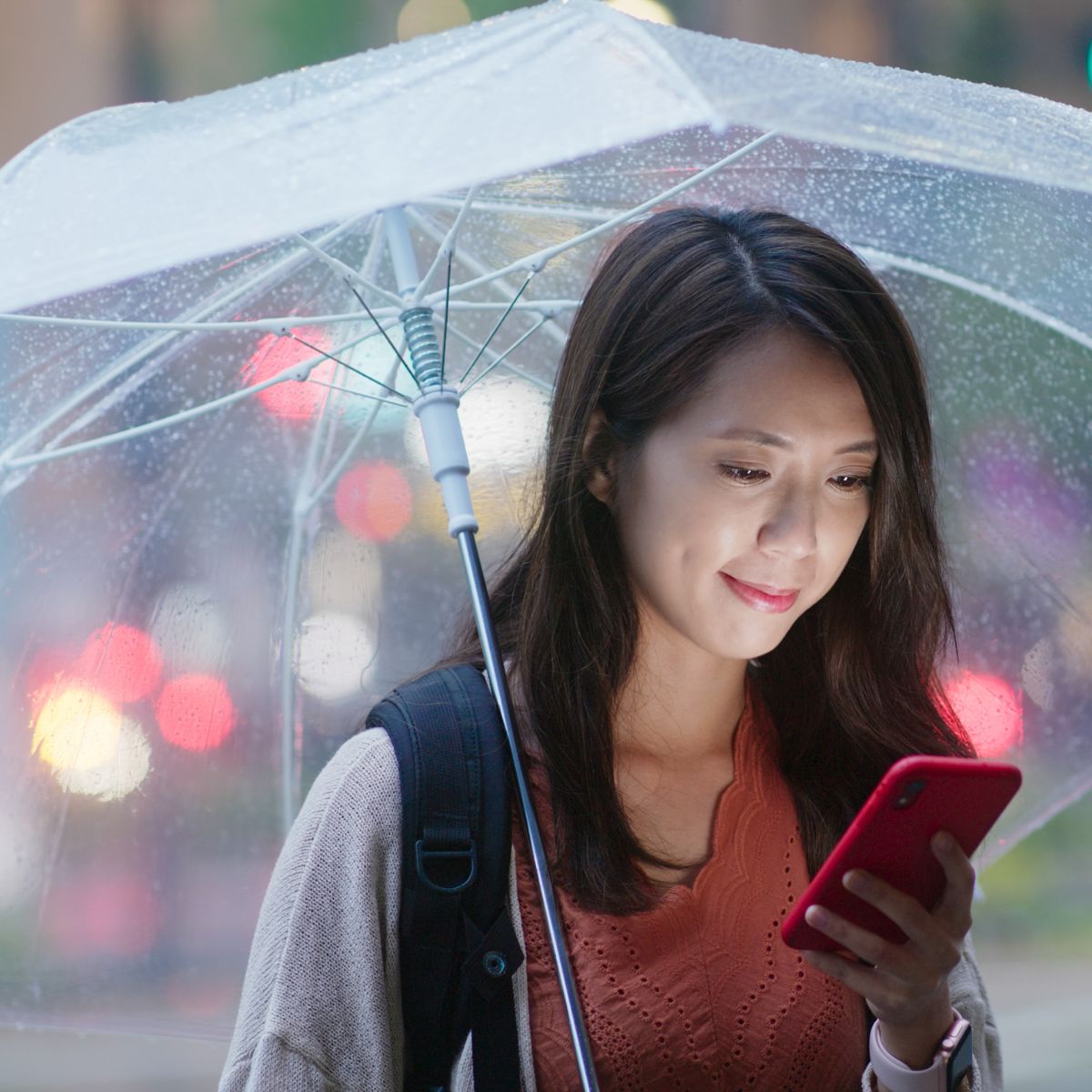 woman holding umbrella in rain and texting on mobile phone